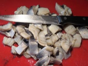 herring fillets cut into pieces, a knife lying beside them, fish ready for making blackcurrant herring