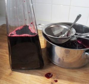 bottle half filled with blackcurrant cordial with sieve and spoon beside the bottle