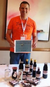 Heiko Danner standing behind a table displaying a huge range of blackcurrant products and holding an award for the overall winner at the blackcurrant contest 2016