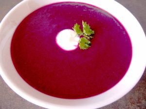round shaped dish with blackcurrant gaspacho, decorated with a little bit of yogurt and parsley
