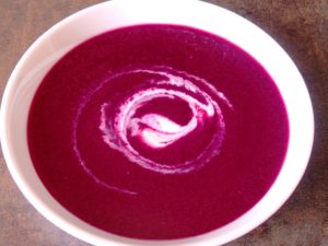 round shaped white dish with blackcurrant and beetroot gaspacho, decorated with white yogurt