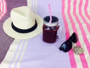 glass of energy blackcurrant smoothie with a hat and sunglasses lying beside