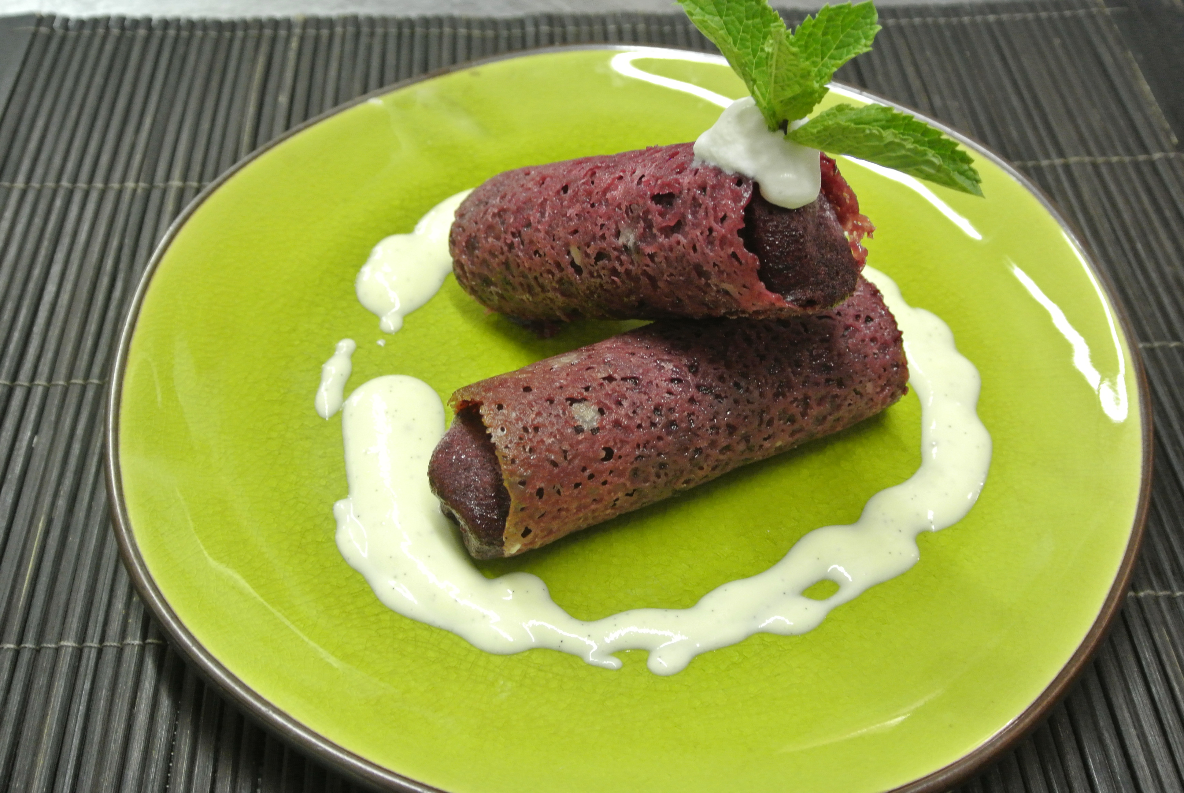 green plate with2 frosted blackcurrant cannelloni garnished with mint leaves and cream