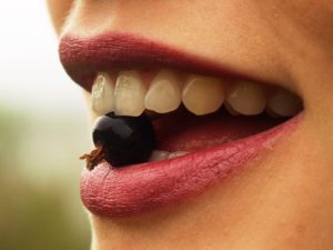 Mouth with teeth holding a blackcurrant