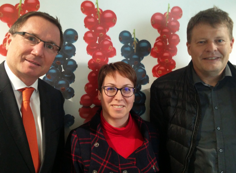 Franz Ennser (CEO Austria Juice), Stefanie Sharma (General Manager IBA) and Jens Holme Pedersen (president IBA) standing in front of a wall decorated with red and blackcurrants, illustrating an article about a meeting in Austria