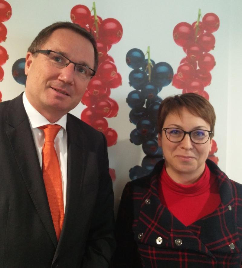 Franz Ennser (CEO Austria Juice), Stefanie Sharma (General Manager IBA) standing in front of a wall decorated with red and blackcurrants, illustrating an article about a meeting in Austria