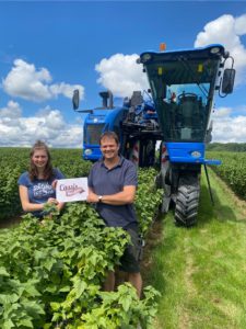 Blackcurrant grower Heiko Danner and his daughter standing in front of a harvester in a blackcurrant field